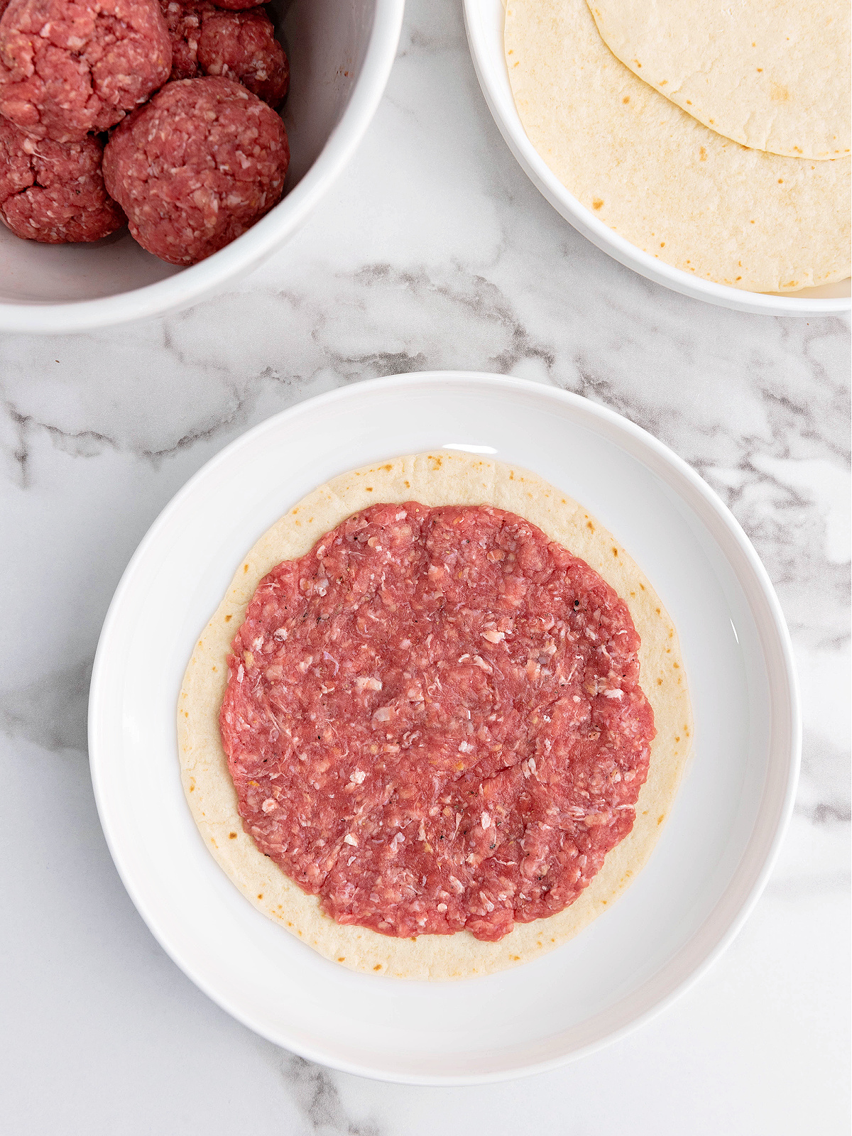A tortilla topped with raw ground beef.