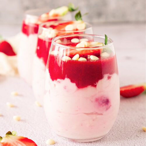 Glass filled with strawberry mousse and topped with a fresh strawberry and white baking chips.