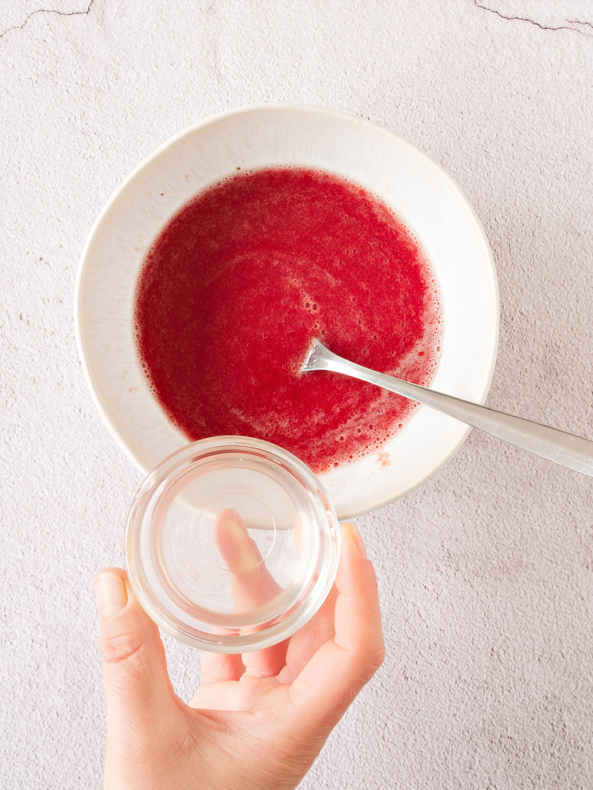 Gelatin being added to a bowl of pureed strawberries.