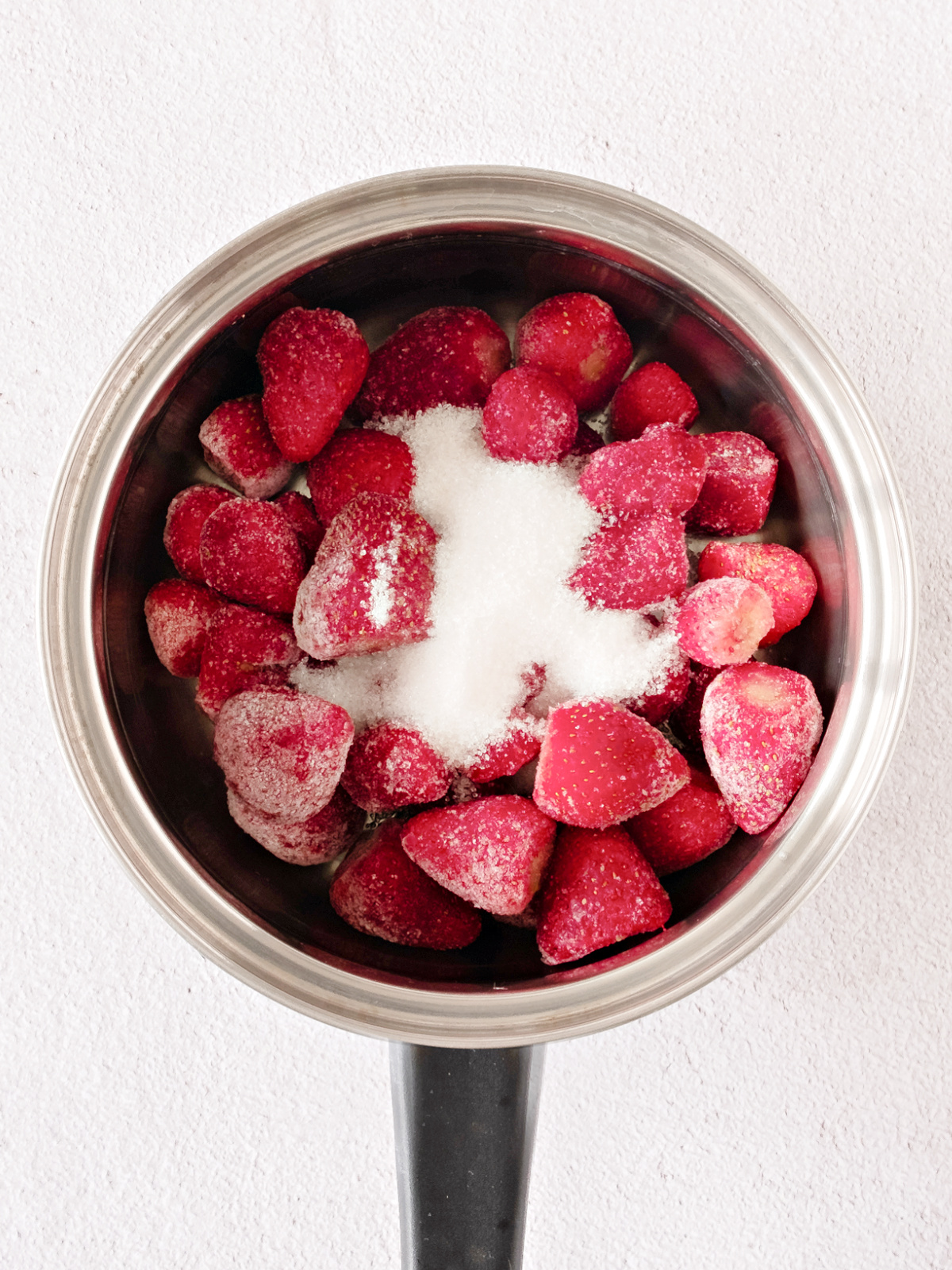 Frozen strawberries in a saucepan topped with sugar.