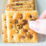 Woman's handing selecting a seasoned cracker on a tray.
