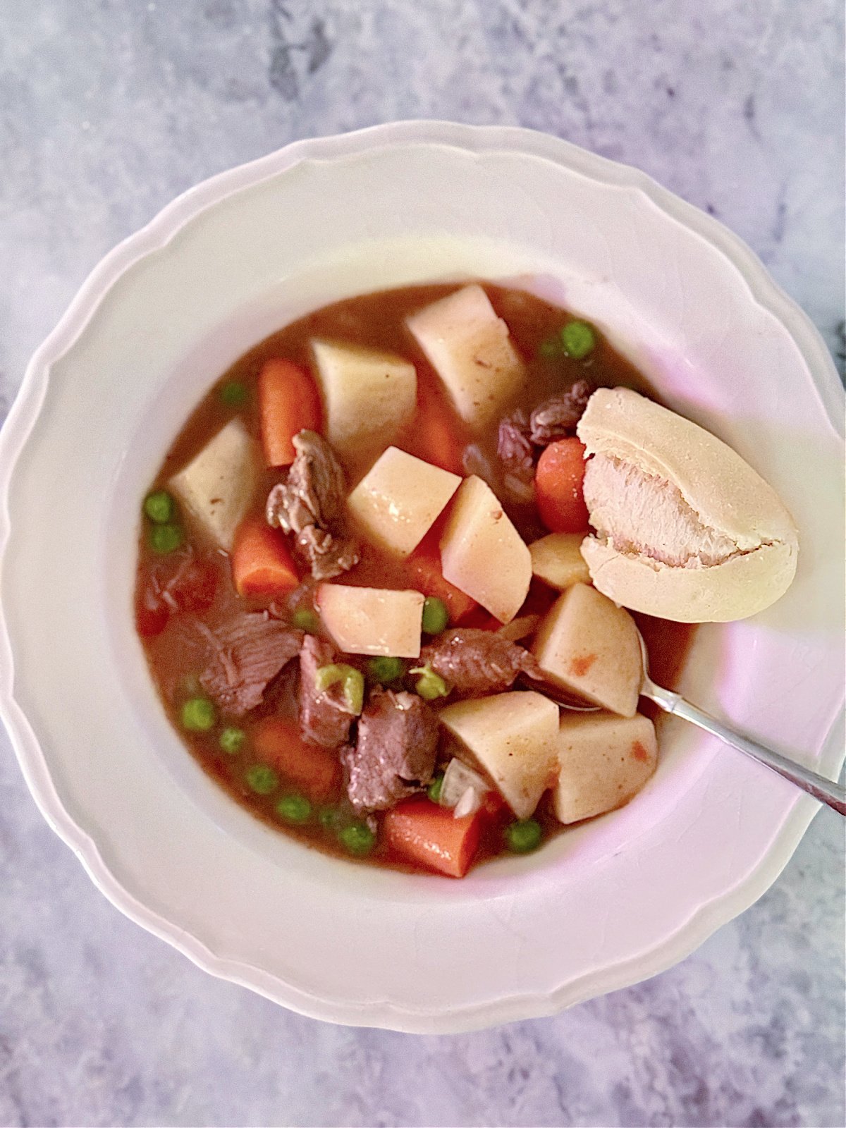 Bowl of beef stew made with potatoes, carrots, English peas, and chunks of beef.