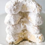 Stack of four powdered sugar covered crescent shaped cookies.