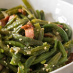 Bowl of green beans seasoned with garlic and bacon pieces.