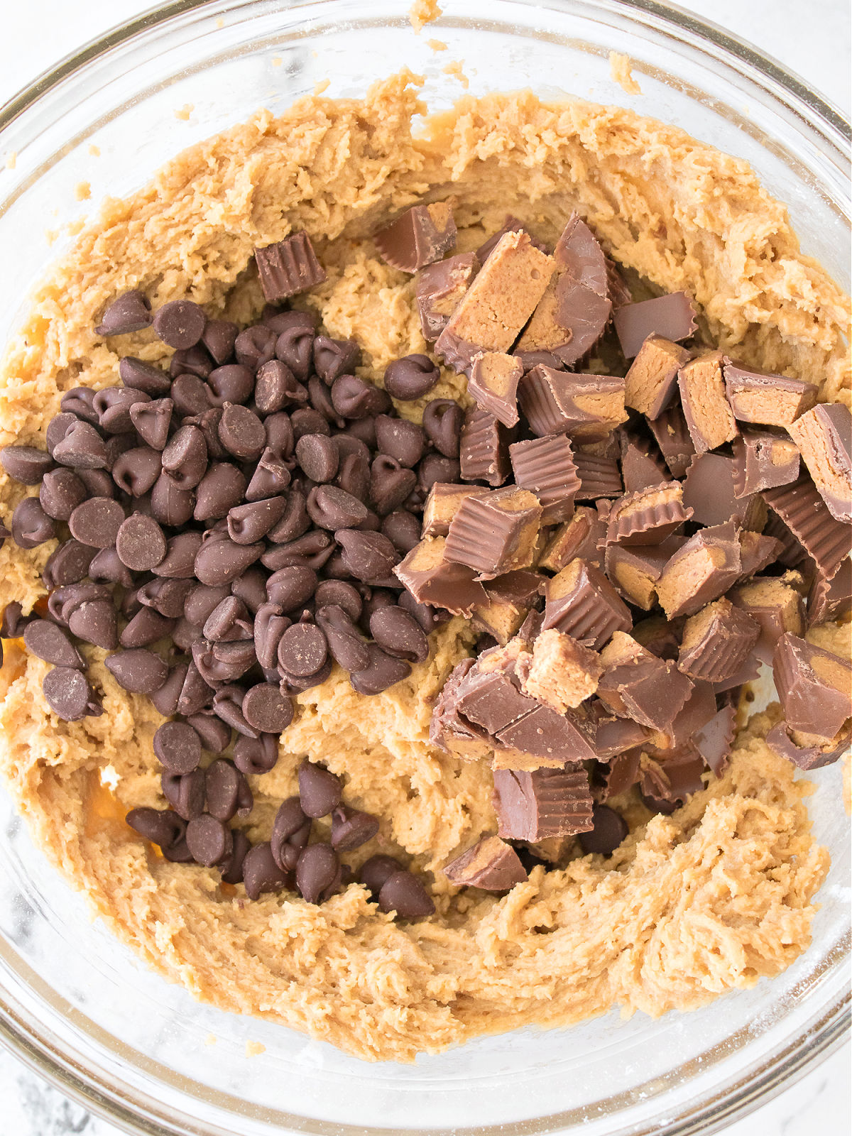 Chocolate chips and cut up Reese's cups on top of batter in a bowl.