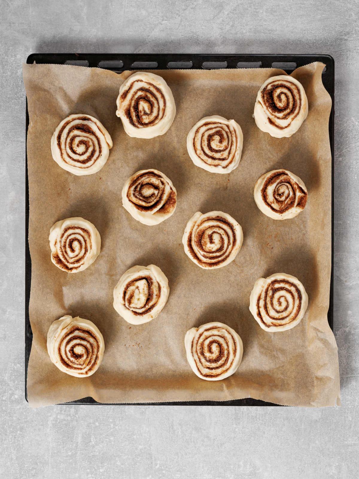Cut cinnamon rolls arranged on a baking sheet before rising.