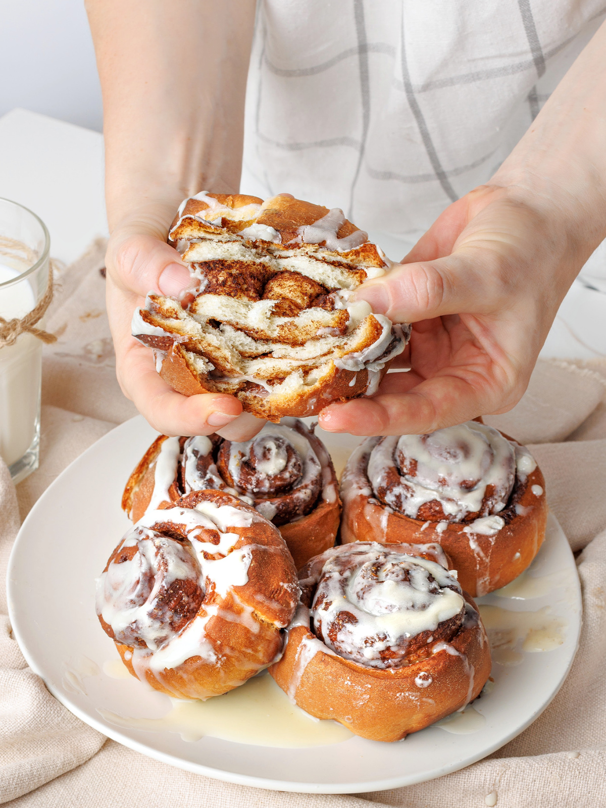 Hand holding an iced cinnamon roll folded in half to show the soft layers and filling.