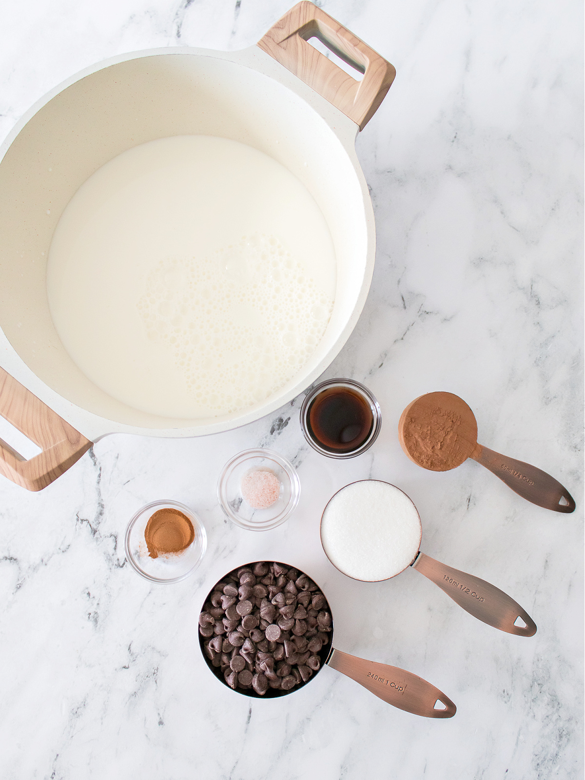 Flat lay of cocoa powder, sugar, milk, vanilla, and chocolate ready to make rich hot chocolate.