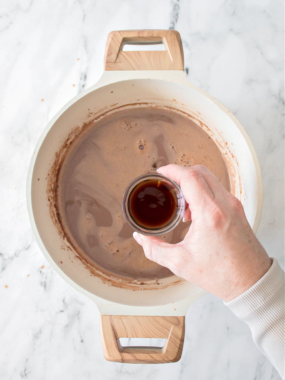 Pure vanilla extract being poured into simmering chocolate milk mixture on the stove.