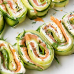 Cucumber, cream cheese, and salmon rolls on a white plate.