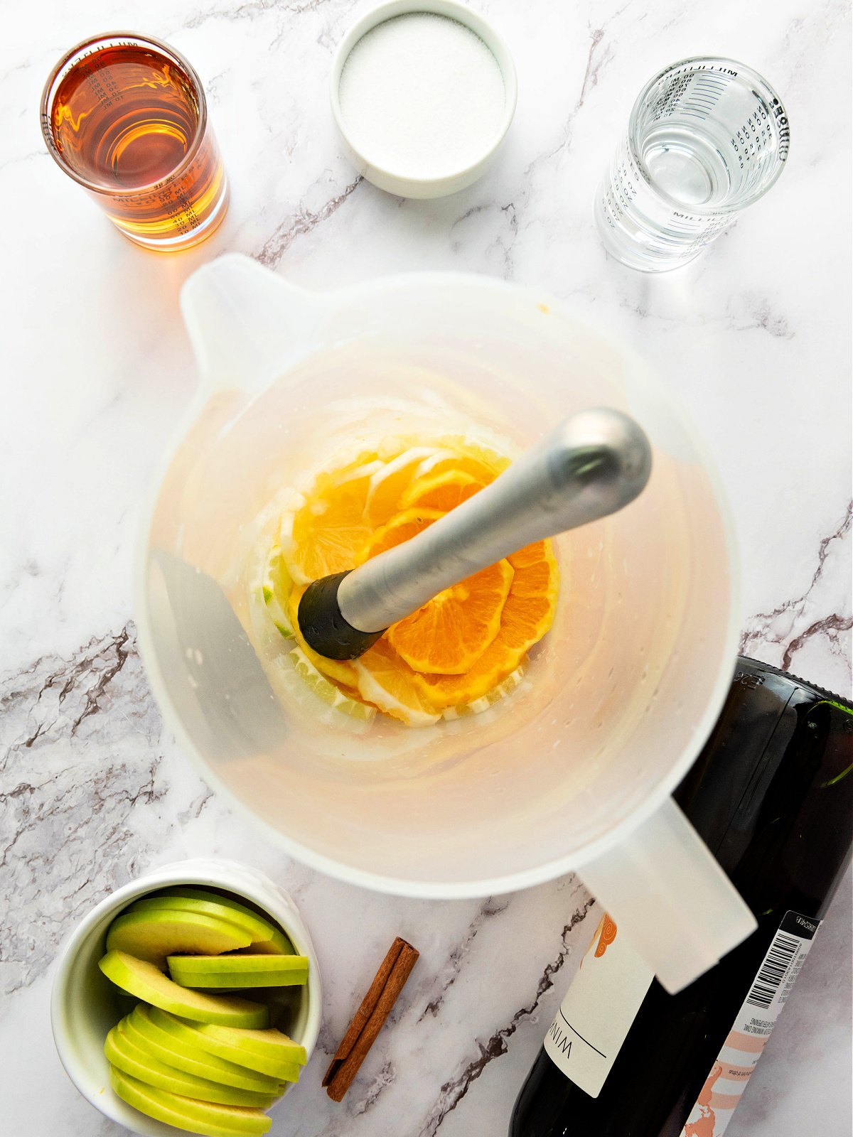 Fruit being muddled in a large pitcher.