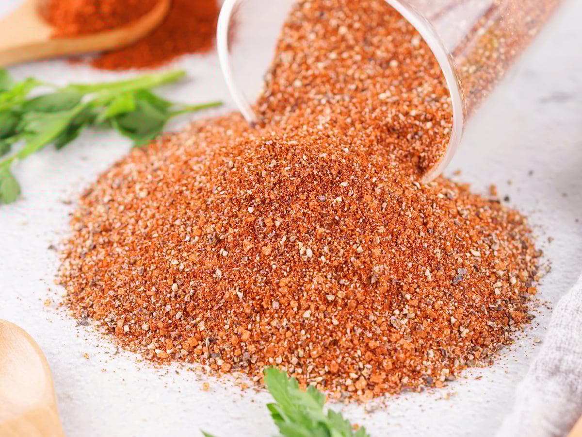 Smoky barbecue spices spilling out of a glass jar.