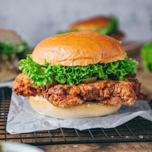 Fried chicken sandwich with curly lettuce, pickles, aioli, and a brioche hamburger bun.