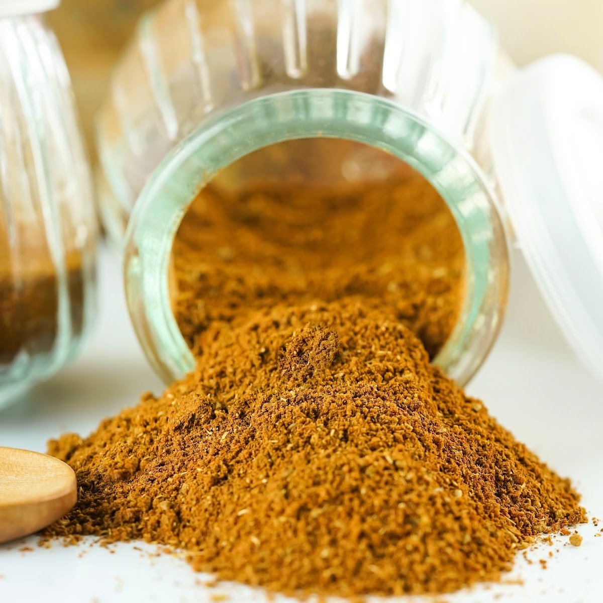 Glass jar of homemade Chinese 5 spice blend spilling onto a table.