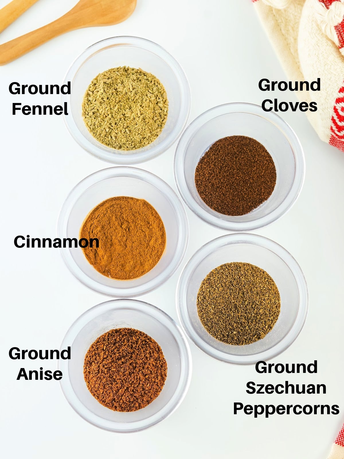 Small bowls filled with star anise, fennel seeds, cloves, cinnamon, and Sichuan peppercorns arranged on a table.