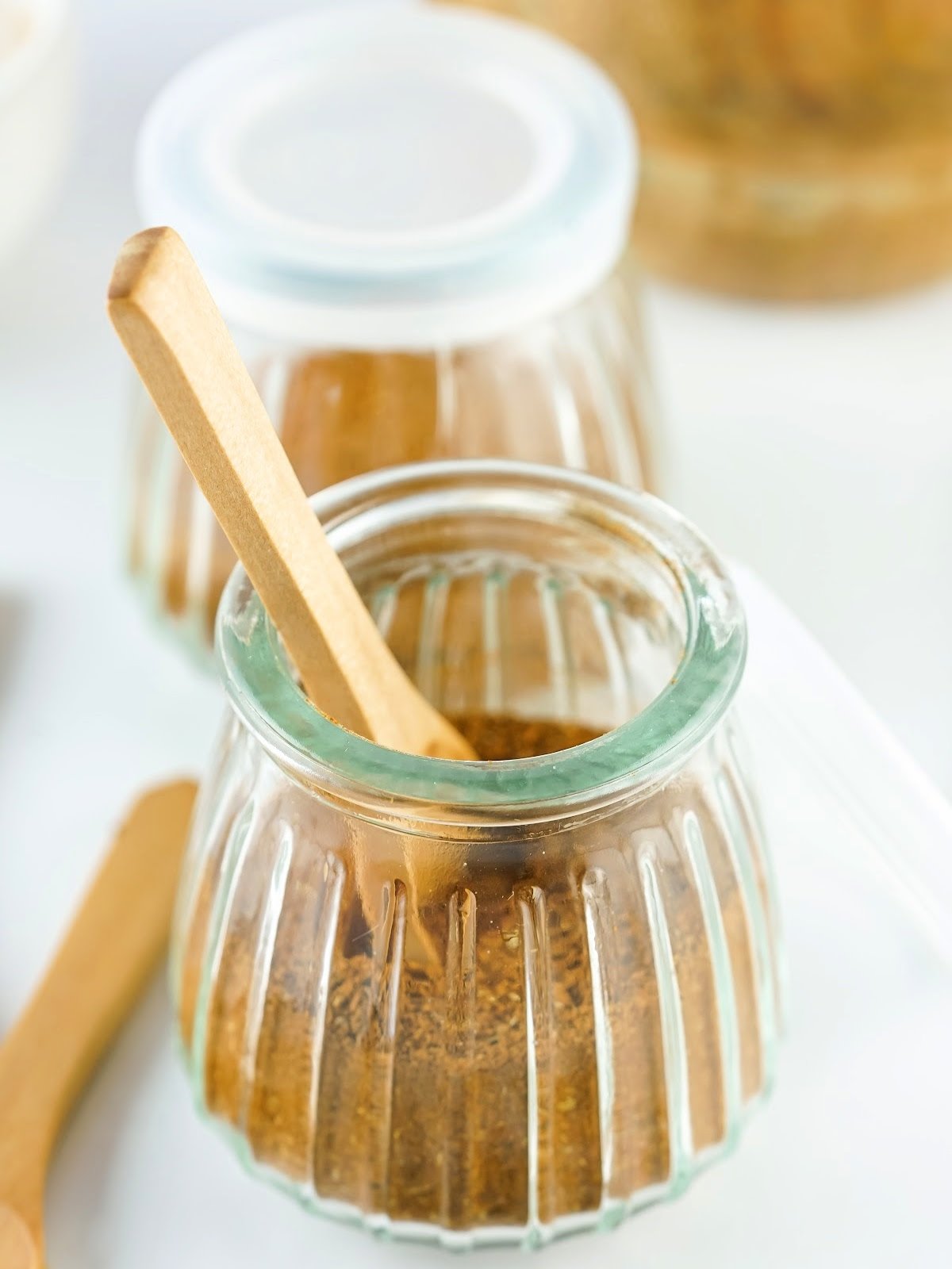Jar of homemade Chinese 5 spice blend with a wooden spoon resting beside it.