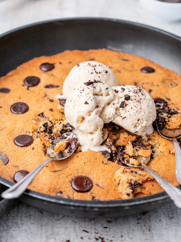 Chocolate chip cookie dough baked in a skillet and topped with vanilla ice cream.