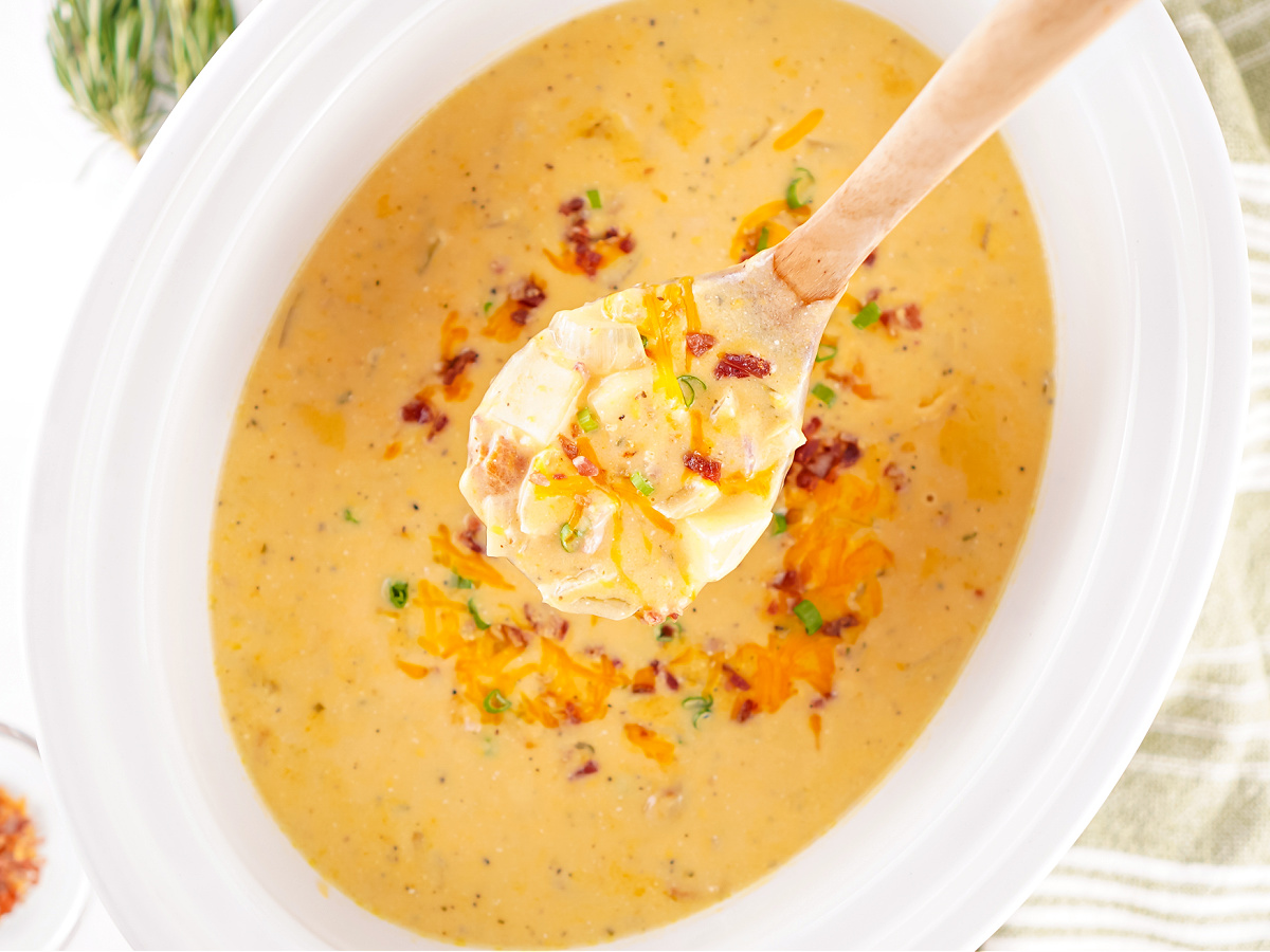 Spoonful of potato soup held above a full crockpot, highlighting the hearty, cheesy texture.