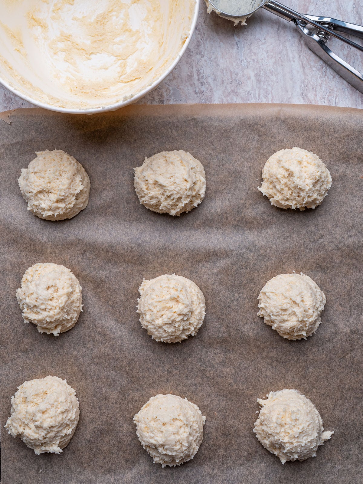Raw buttermilk drop biscuit dough mounds placed on a baking sheet ready for the oven.