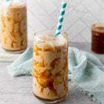 Glass of iced caramel coffee served on a rustic wooden table with a straw.