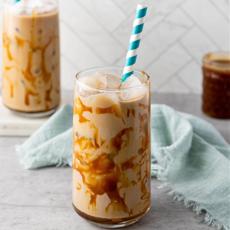 Glass of iced caramel coffee served on a rustic wooden table with a straw.