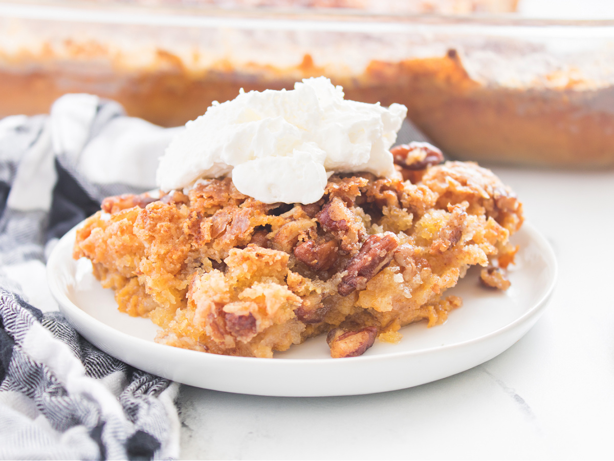 Slice of Pumpkin Crunch Cake on a plate crowned with fluffy whipped topping, ready to enjoy.