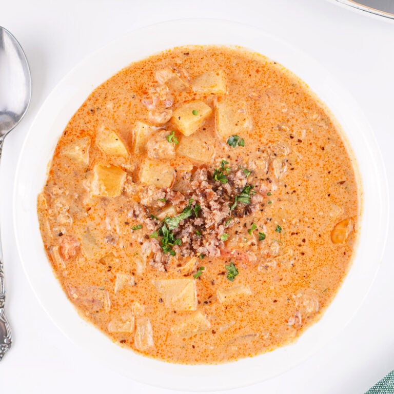 Overhead view of a single bowl of creamy sausage and potato soup with chunks of potato and sausage in a rich broth.