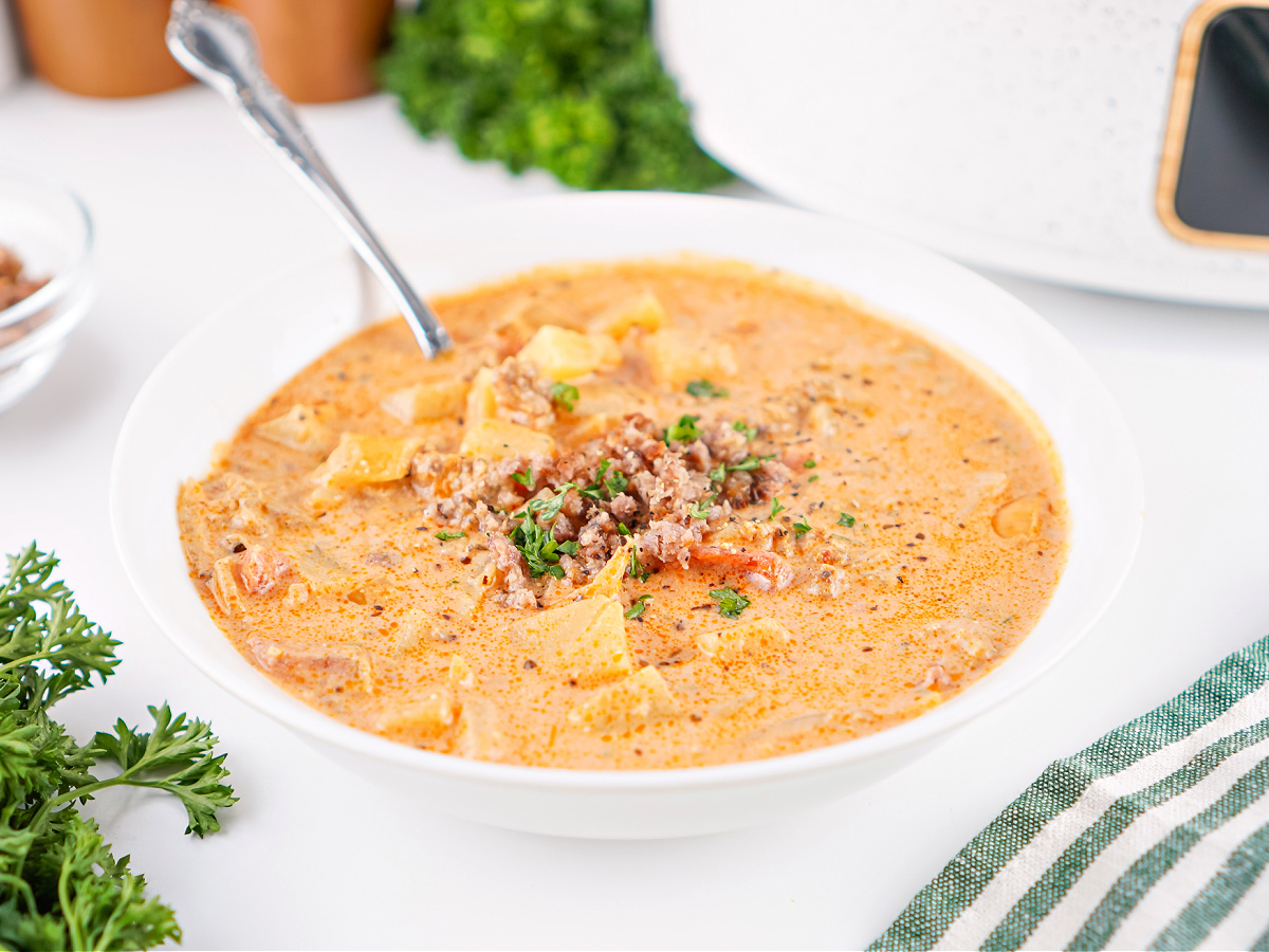Side view of a warm bowl of sausage and potato soup, garnished with herbs and ready to serve.