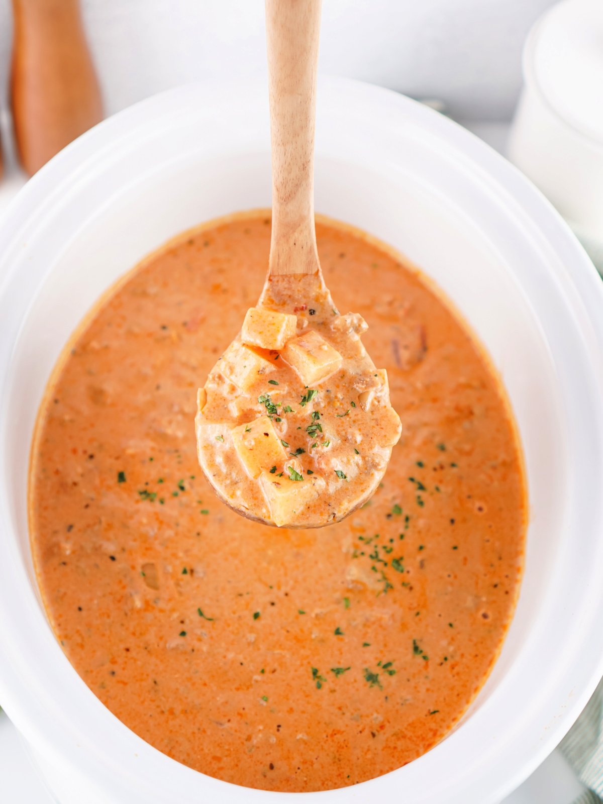 Ladle filled with hearty sausage and potato soup, brimming with creamy broth, potatoes, and browned sausage pieces.
