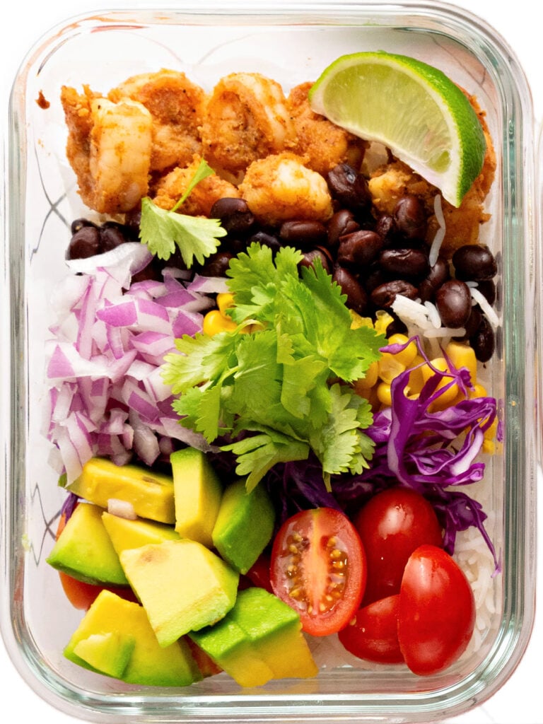 Shrimp, black beans, avocado, tomatoes, red onions, and lime in a glass dish.