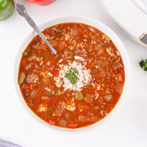 Overhead view of a steaming bowl of Unstuffed Pepper Soup with a spoon resting inside, highlighting tender vegetables and grains of rice.