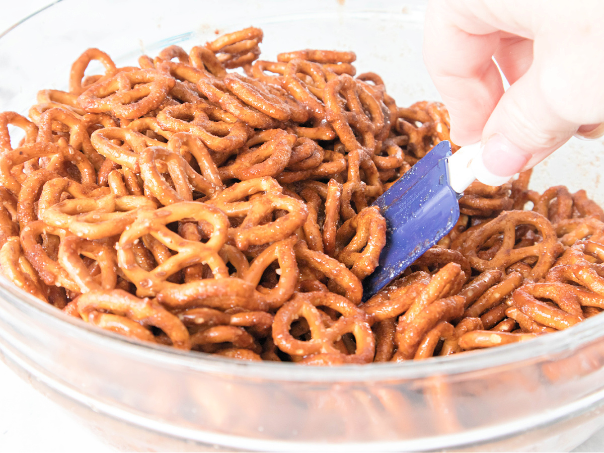 A spatula stirring pretzels in the cinnamon sugar mixture inside a bowl.