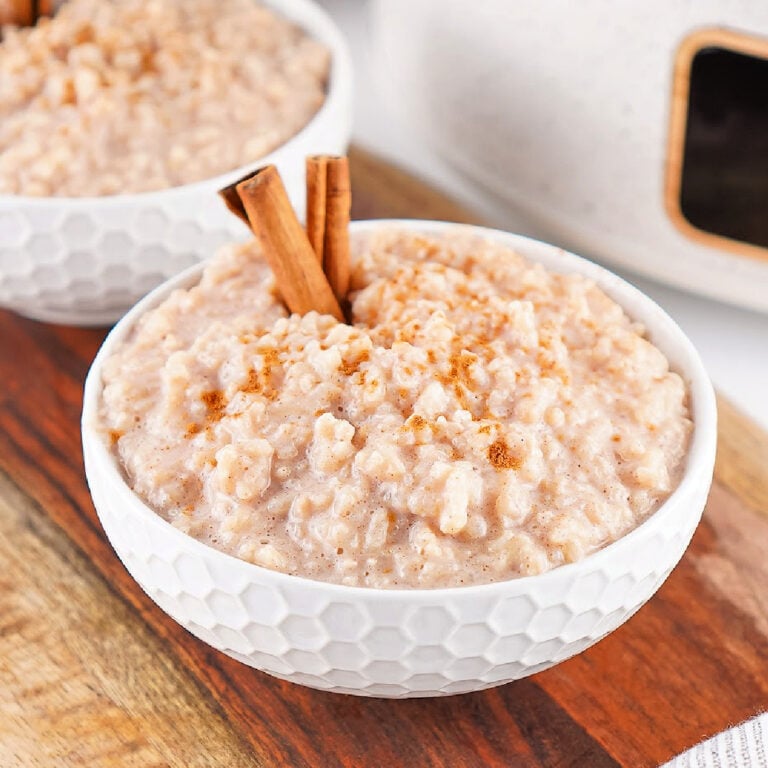 Bowl of creamy Crockpot rice pudding topped with cinnamon and garnished with cinnamon sticks.