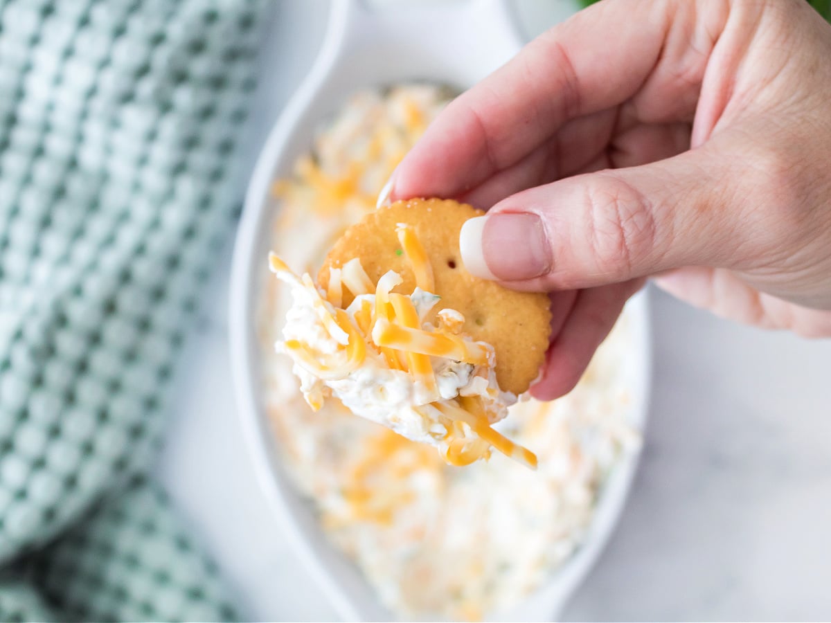 A woman holding a Ritz cracker topped with jalapeño cream cheese dip.