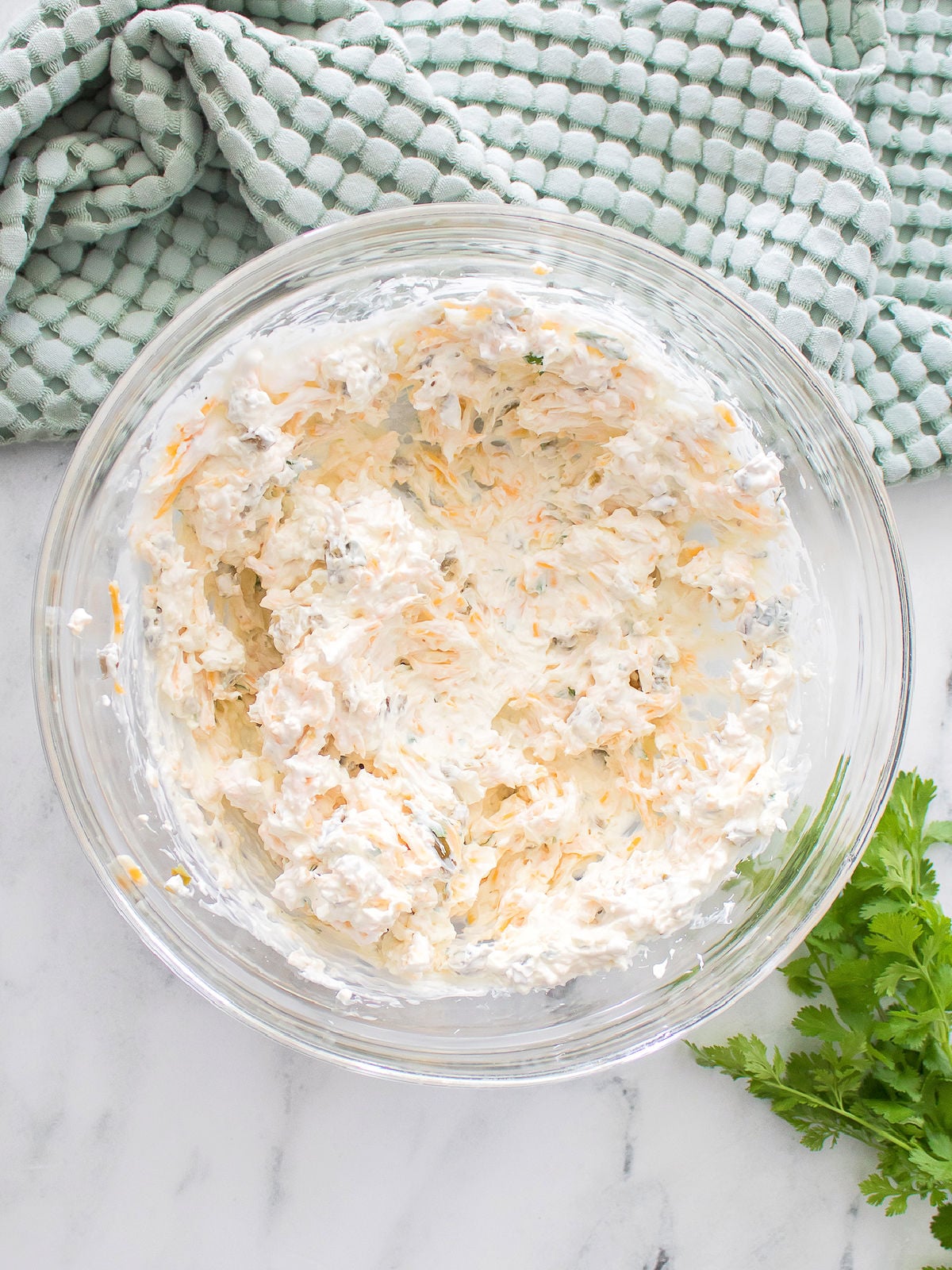 Cream cheese, jalapeños, and seasonings mixed together in a clear glass bowl.