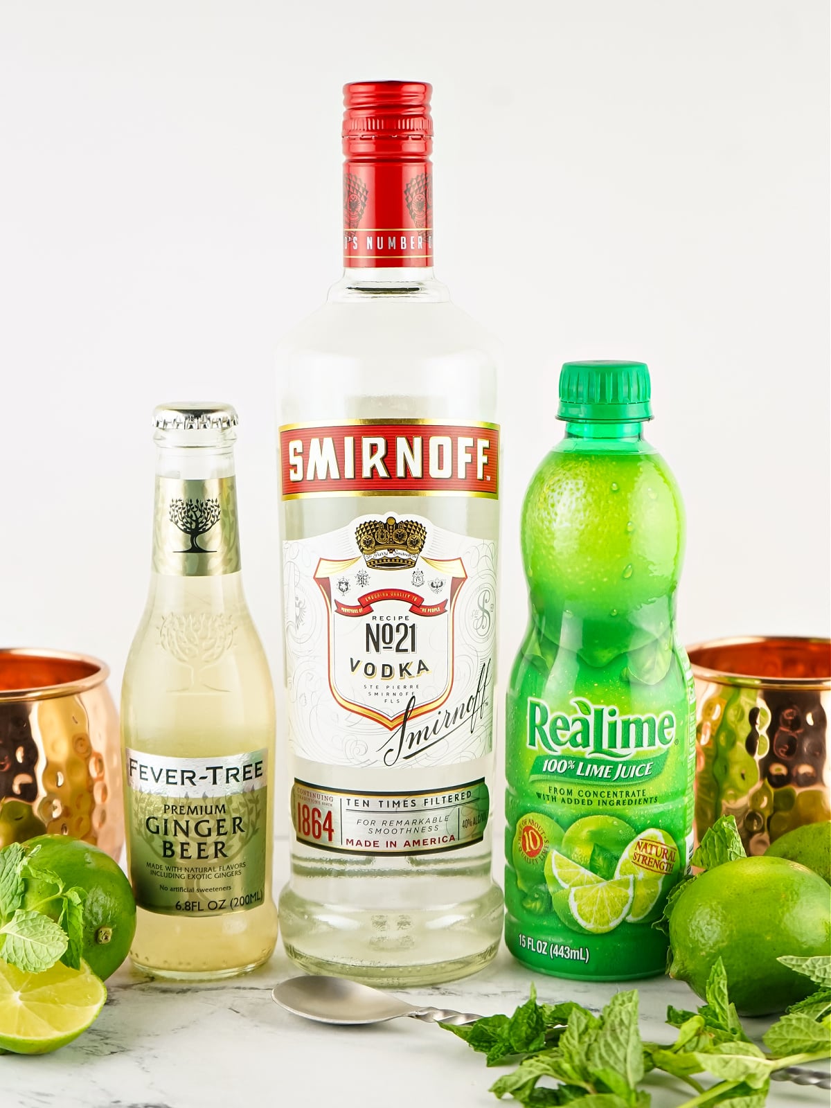 Fresh ingredients laid out to make a classic Moscow Mule: vodka, lime, mint, and ginger beer.
