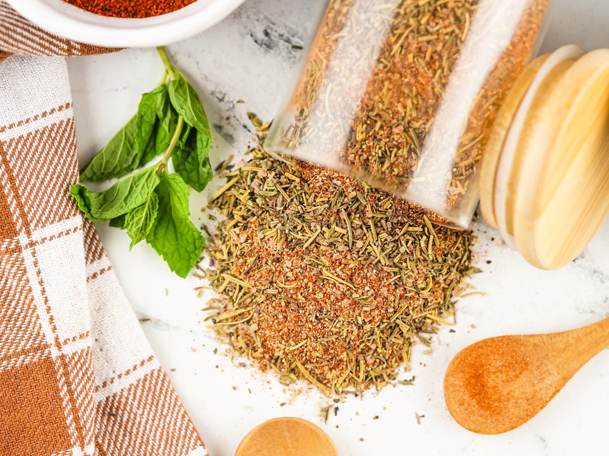 A glass jar tipped over with turkey rub spilling onto a countertop.