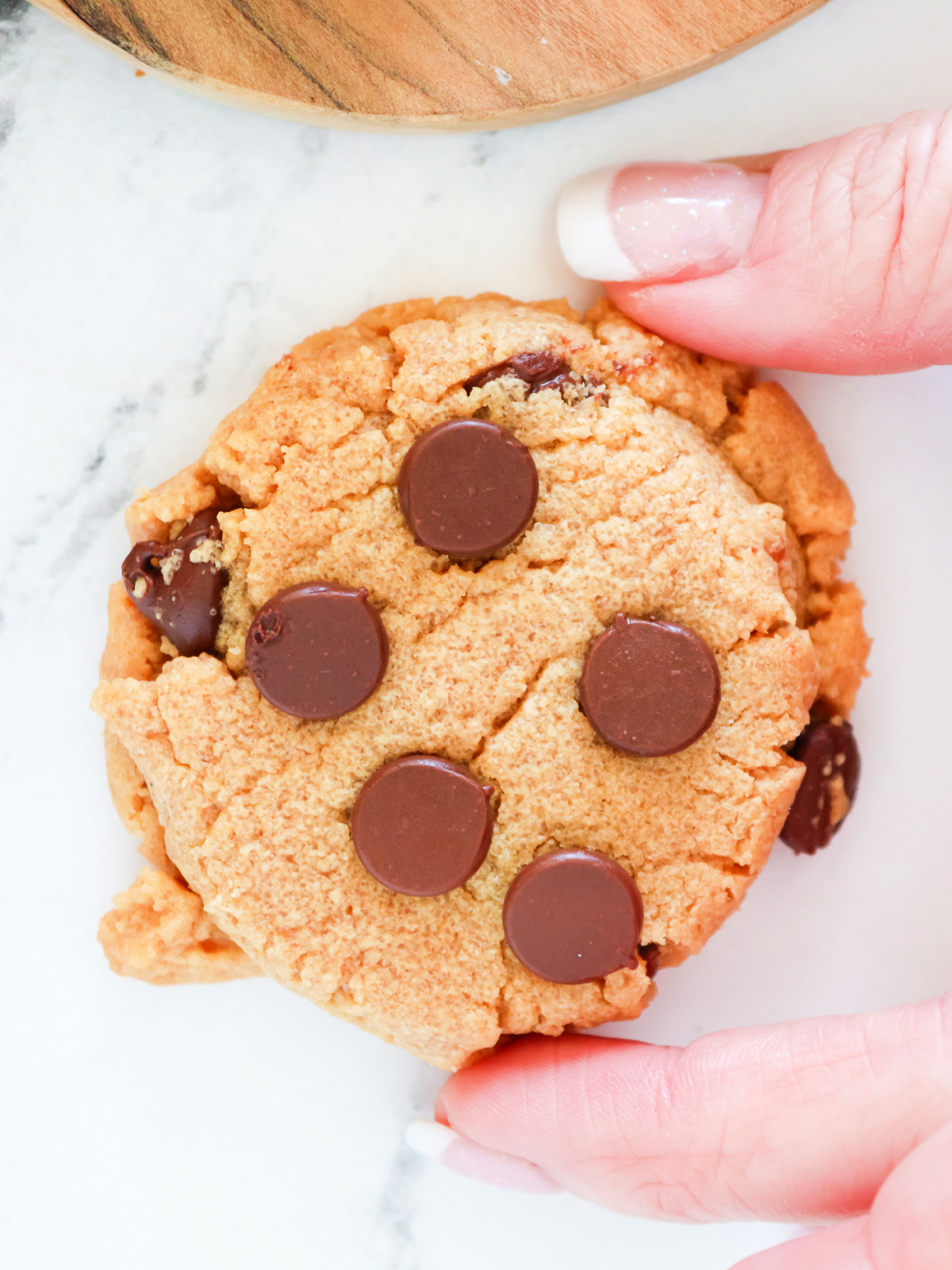 A hand holding a soft peanut butter cookie studded with melted chocolate chips.