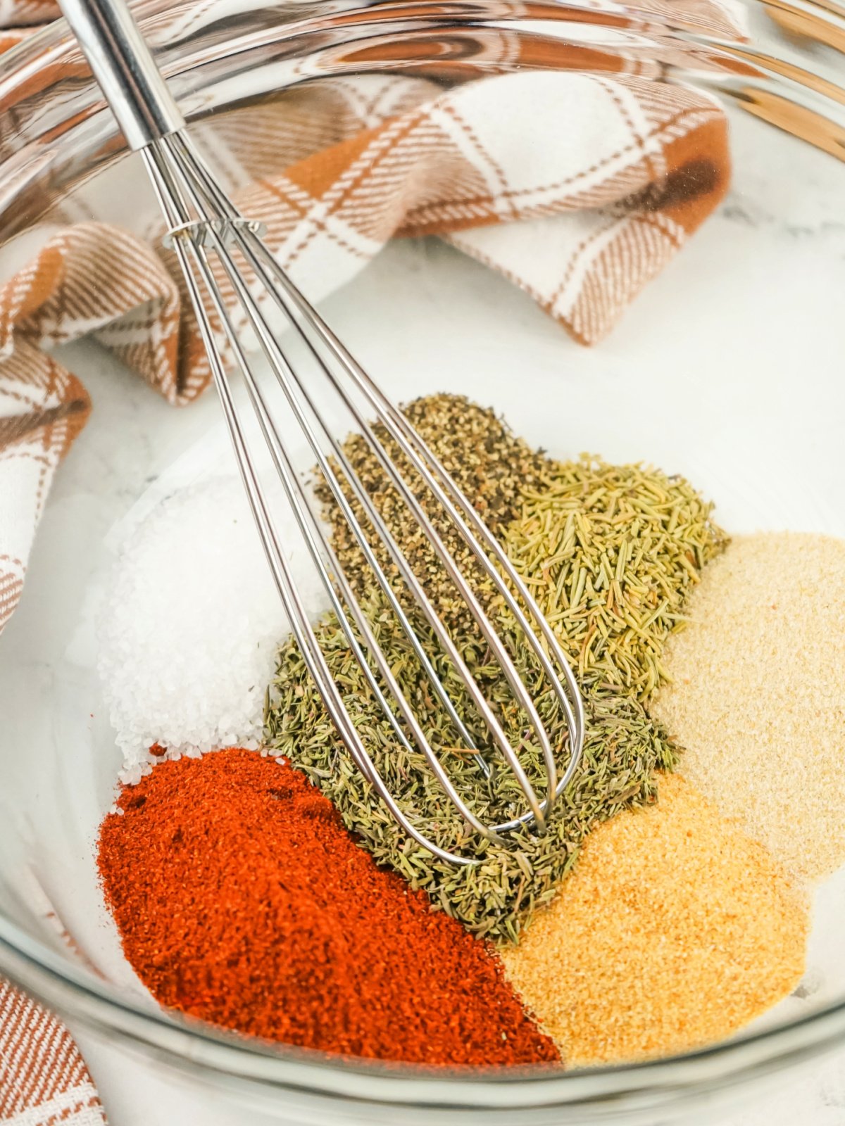 A whisk mixing colorful herbs and spices in a glass bowl to make turkey rub.