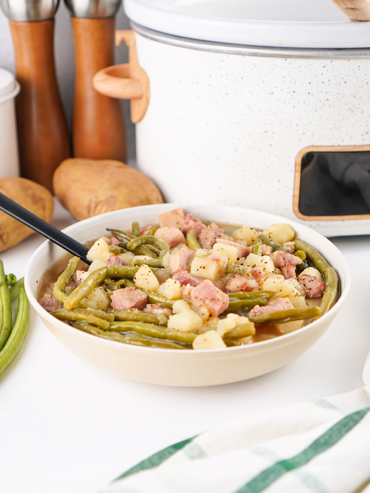A close-up of a bowl of ham, green beans, and potatoes with a spoon, showcasing the tender beans, soft potatoes, and smoky ham in every bite.