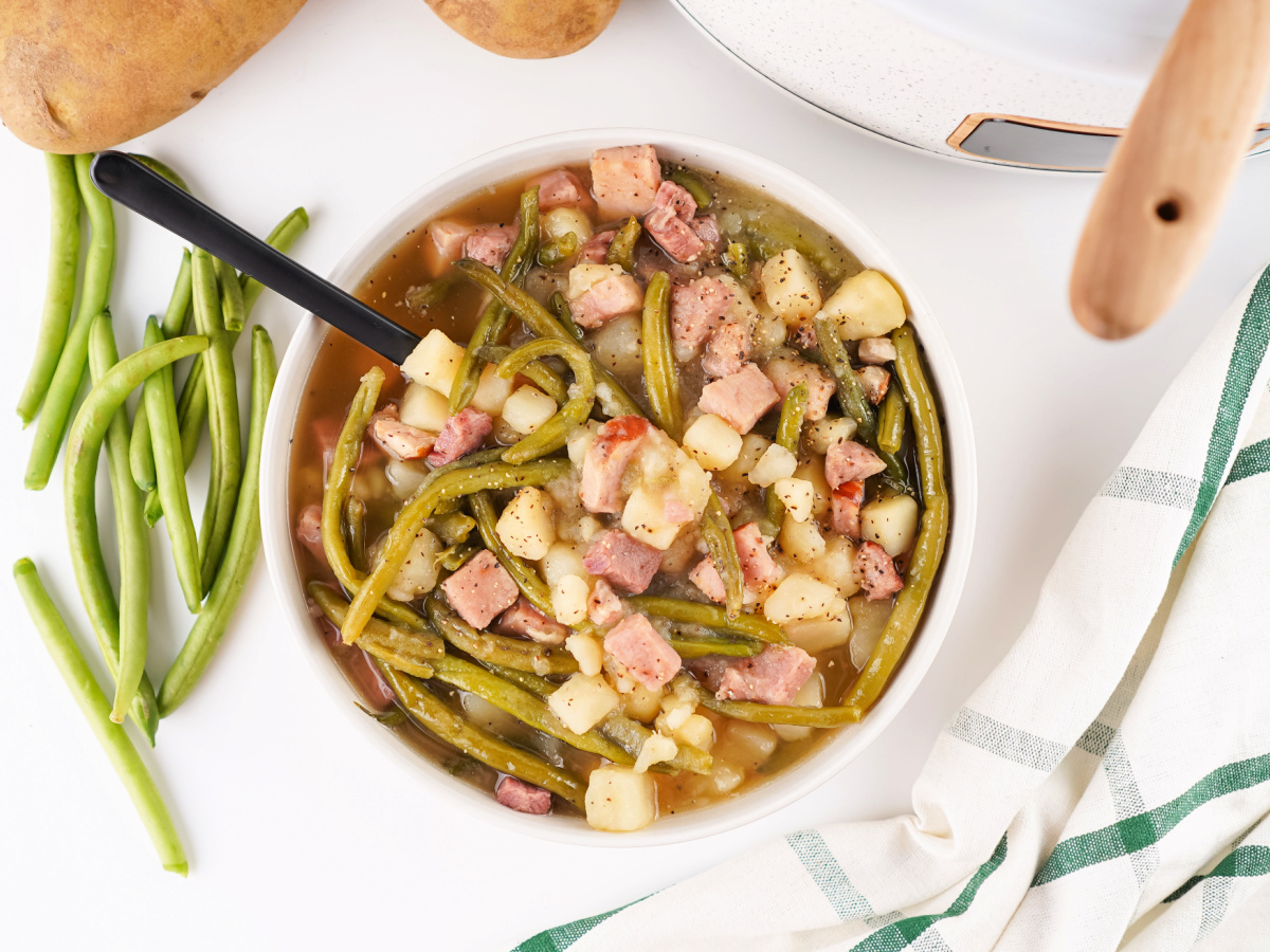 A bowl filled with slow-cooked ham, green beans, and potatoes in a flavorful broth, ready to serve.