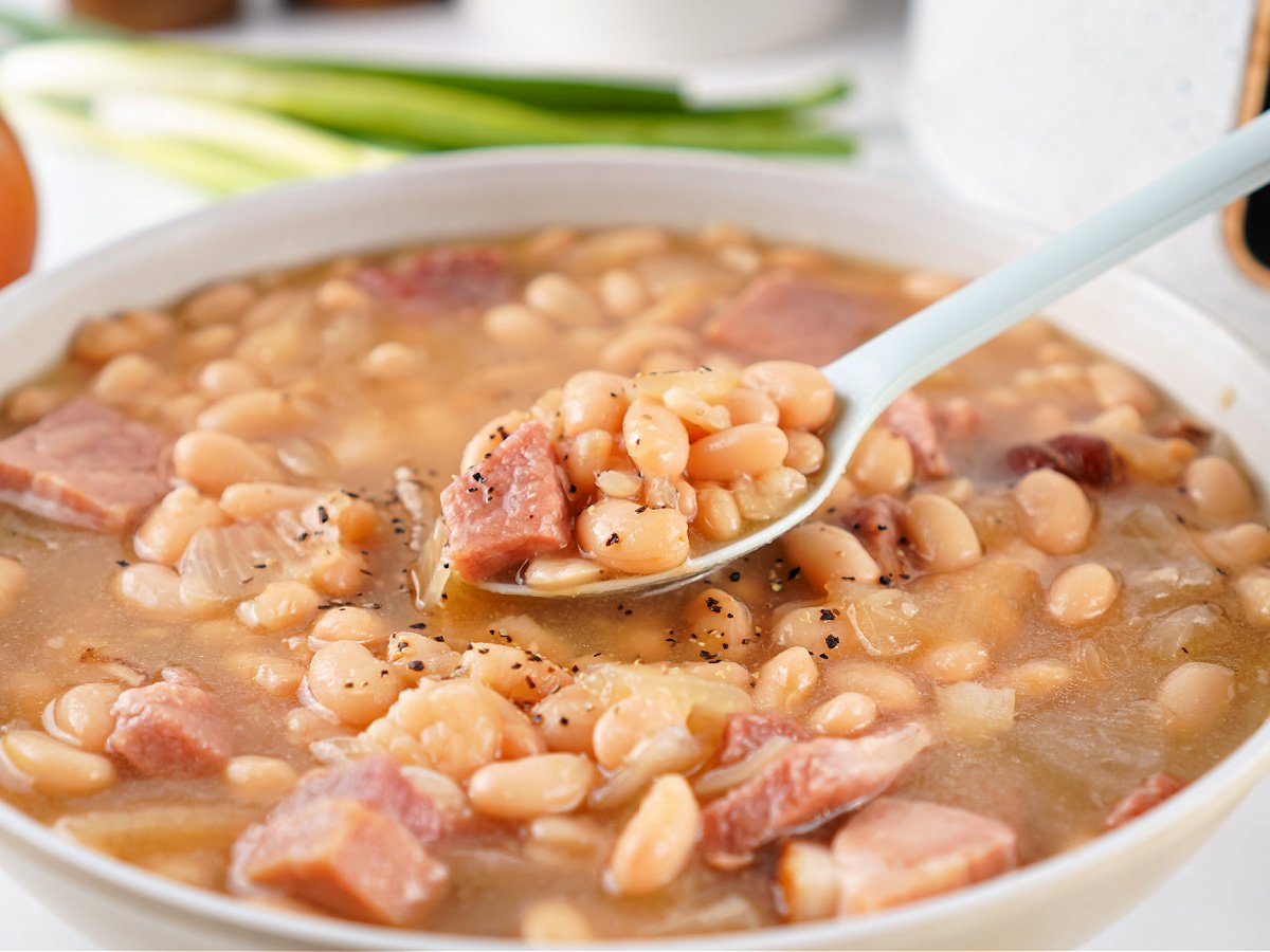 Close-up of a spoonful of ham and bean soup with tender beans, smoky ham, and rich broth for a cozy meal.