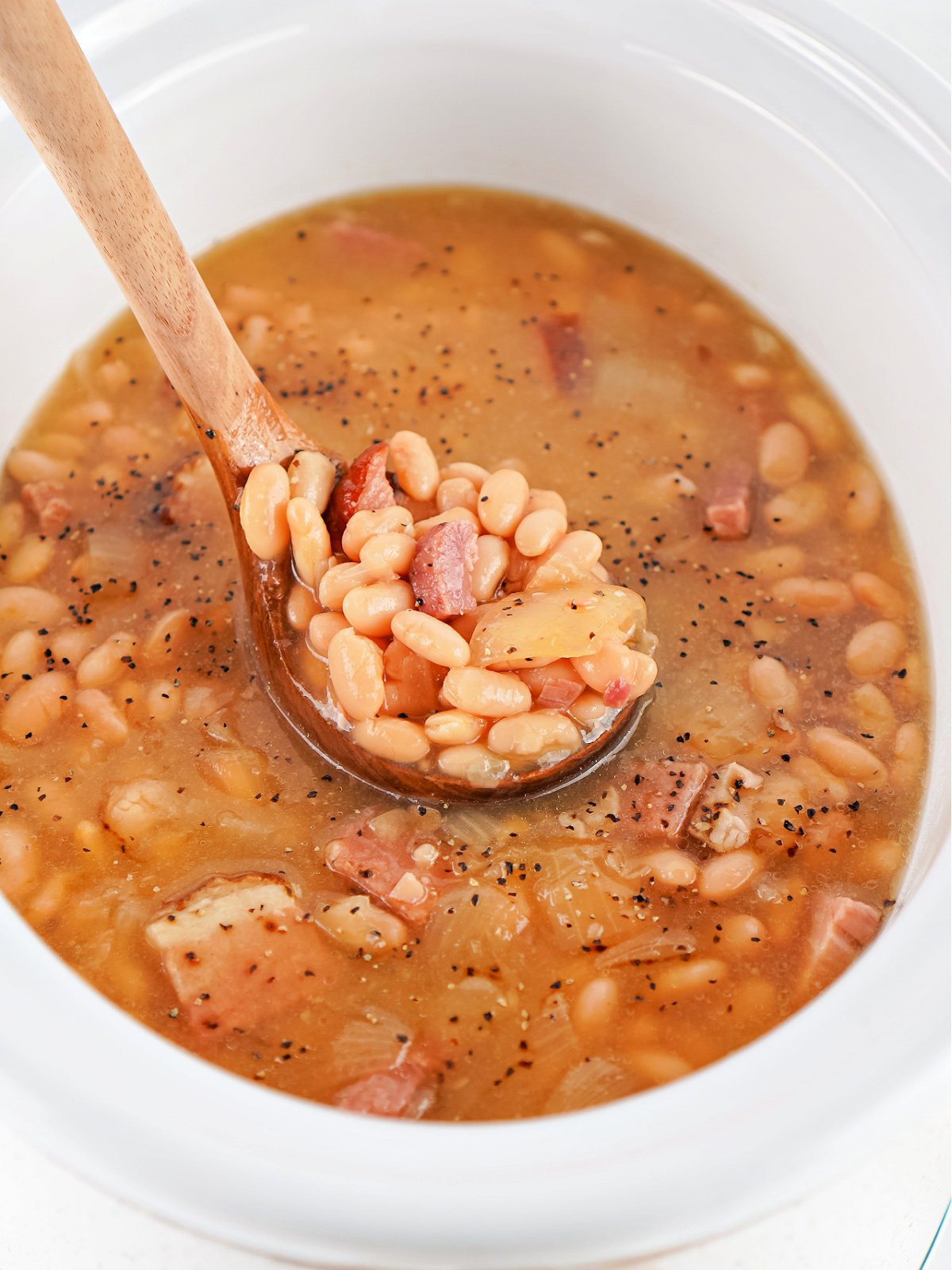 A ladle scooping hearty Crockpot ham and bean soup, showing chunks of ham, beans, and vegetables in savory broth.