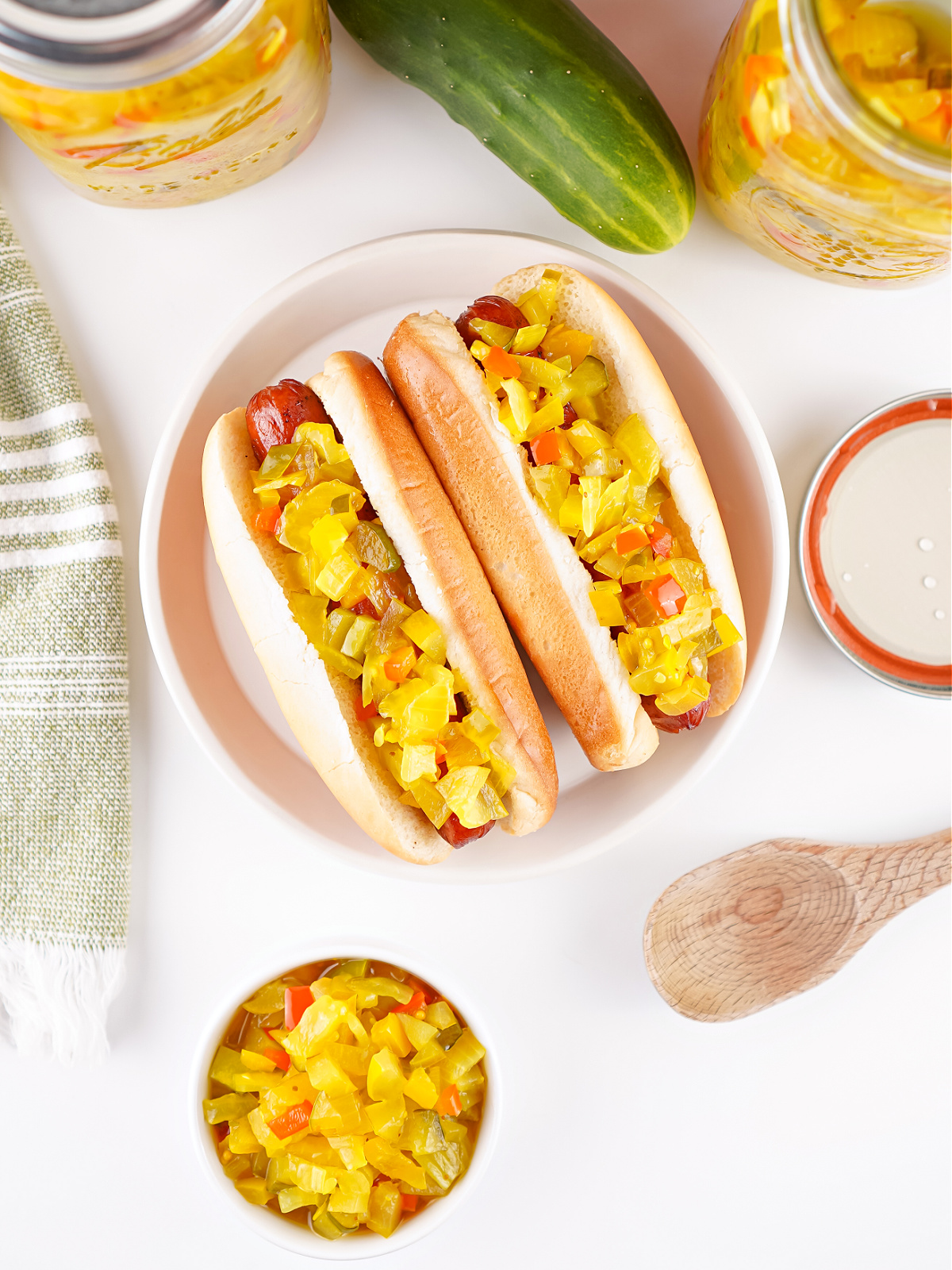Hot dogs topped with sweet pickle relish served on a plate, with jars of relish in the background.