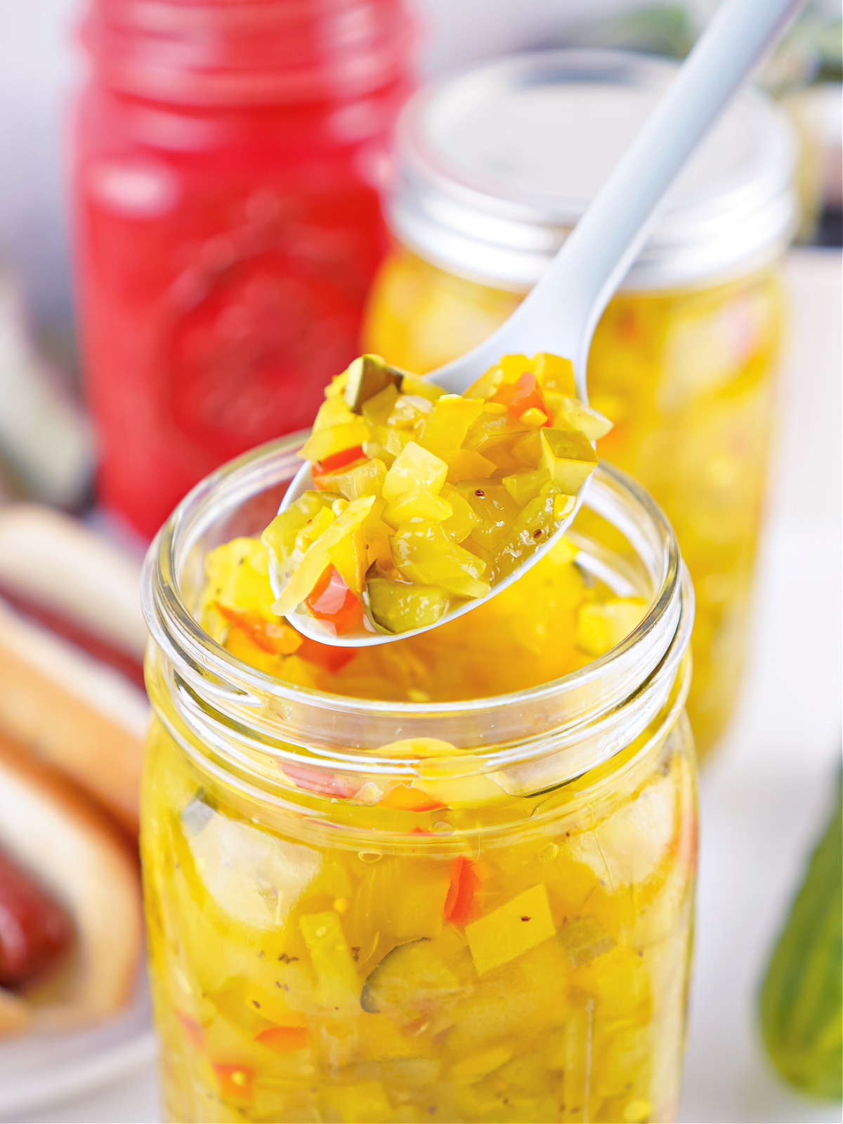 Close-up of sweet pickle relish on a spoon above an open jar, showing chopped cucumbers and peppers.