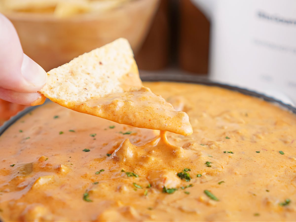 Tortilla chip dipped into creamy taco queso dip with ground beef.