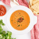 Creamy taco queso dip with ground beef and salsa served warm in a crockpot, garnished with herbs.