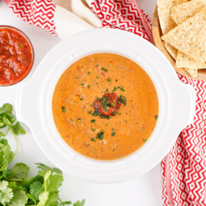 Creamy taco queso dip with ground beef and salsa served warm in a crockpot, garnished with herbs.