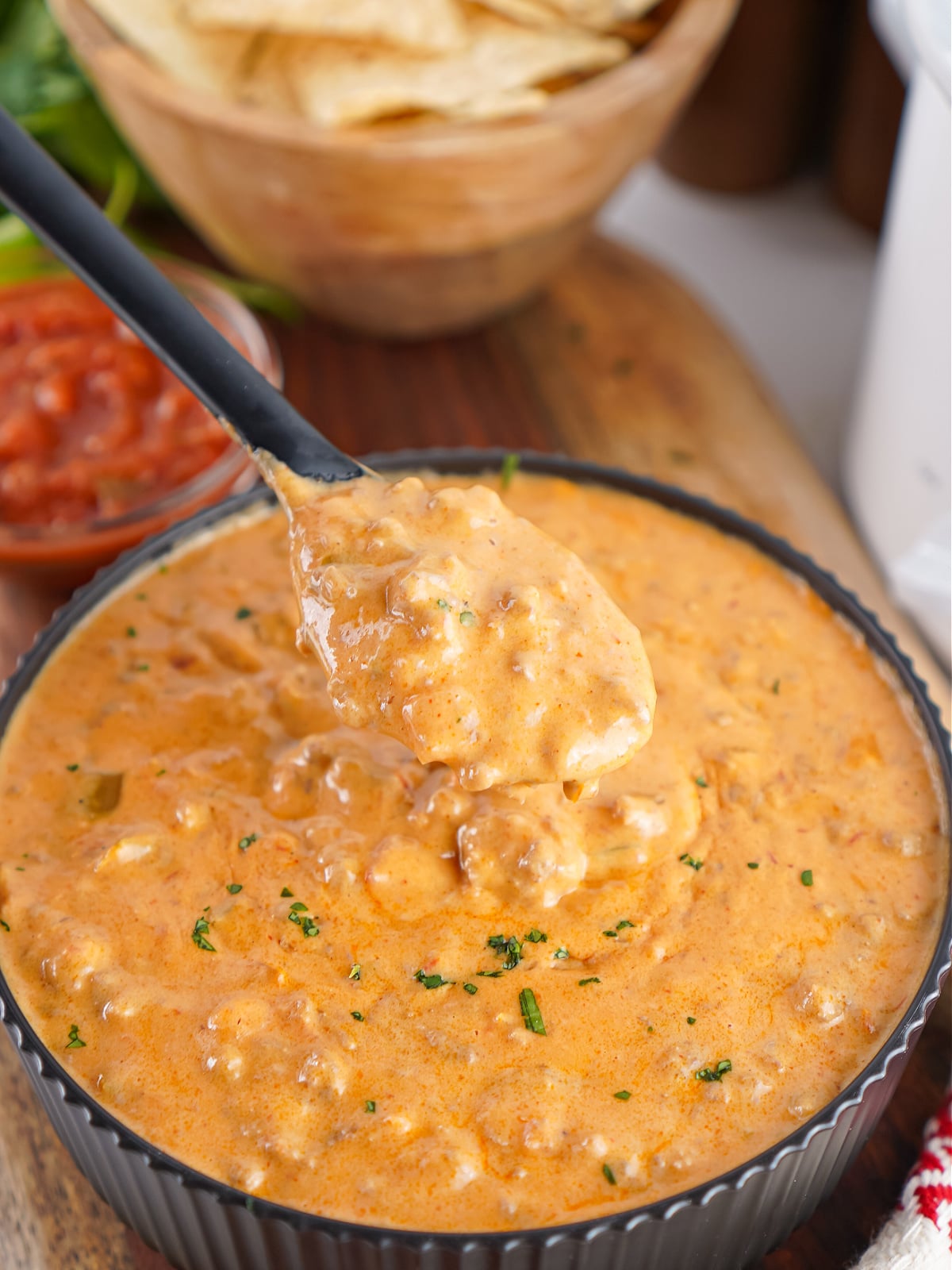 Spoon lifting thick taco queso dip with ground beef from a serving bowl.