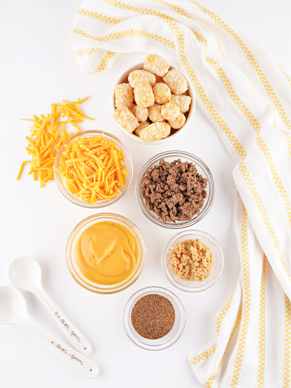 Ingredients for crockpot taco tater tot casserole including ground beef, shredded cheddar cheese, cheese sauce, taco seasoning, and frozen tater tots.